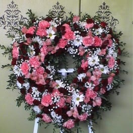 Heart-shaped floral wreath on an easel with pink, white, and red flowers