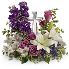 Purple and white floral arrangement with roses, lilies, and a silver cross