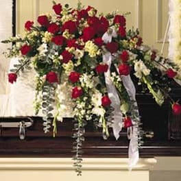 Red and white casket spray of roses and white flowers with ribbons on a dark wood casket