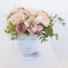 Blush roses and an orchid arranged in a white vase with pearl accents