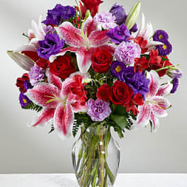 Bouquet of red roses, pink lilies, and purple flowers in a glass vase