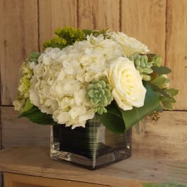 White hydrangeas and roses arranged in a square glass vase