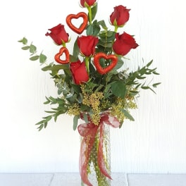 Tall bouquet of red roses in a clear glass vase with heart decorations