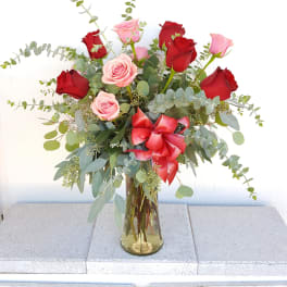 Red and pink roses in a glass vase with a red ribbon
