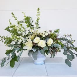 White floral arrangement in a white urn with long greenery