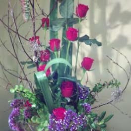 Tall arrangement of pink roses and purple flowers in a black container