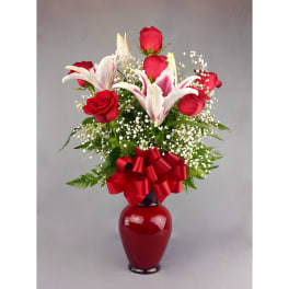 Red roses and white lilies in a red vase with a ribbon bow