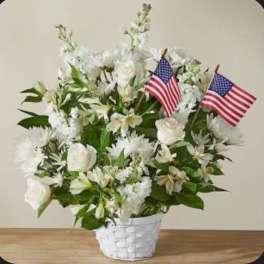 White floral arrangement in a white basket with two small American flags