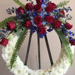 Heart-shaped floral wreath with red roses, blue flowers, and white chrysanthemums