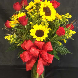 Bouquet of red roses and yellow sunflowers in a glass vase with a red bow