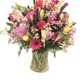 Mixed bouquet of pink, purple, and yellow flowers in a glass vase