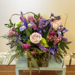 Mixed bouquet of purple, pink, and pale roses in a square container