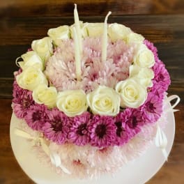 Round floral cake with white roses, pink daisies, and two candles