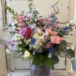 Mixed pastel bouquet in a purple vase with roses and delphinium