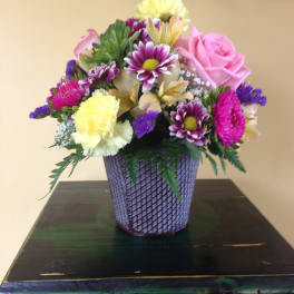 Mixed bouquet in a purple woven vase with pink and yellow blooms
