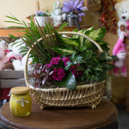 Basket arrangement with green foliage and pink flowers beside a yellow jar candle