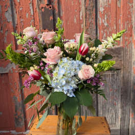 Mixed bouquet in a glass vase with pink roses, blue hydrangea, and tulips