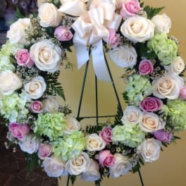 Heart-shaped wreath of white and pink roses on a stand with a white bow