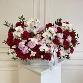 Large arrangement of red roses, pink peonies, and white orchids in a white vase