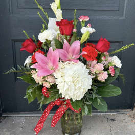 Bouquet of pink lilies, red roses, and white hydrangea in a glass vase