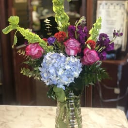 Mixed bouquet with pink roses, blue hydrangea, and purple flowers in a glass vase