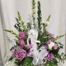 Purple and white floral arrangement with an angel figurine in a basket