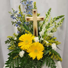 Yellow gerberas and white flowers arranged around a wooden cross
