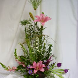 Tall floral arrangement with pink lilies and purple tulips in a dark container