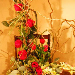 Tall arrangement of red roses in a dark container with curly branches