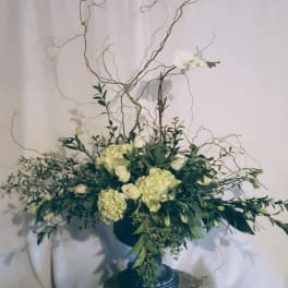 White floral arrangement in a dark pedestal vase with curly branches