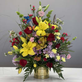 Mixed bouquet with yellow lilies, red roses, and a gold vase