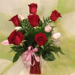 Red roses and pink tulips in a red vase with a pink ribbon