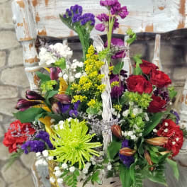 Colorful mixed flower basket with red roses, green spider mum, and purple blooms in a white woven basket.