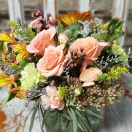 Peach roses and mixed flowers arranged in a square glass vase