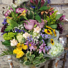 Tall mixed bouquet of roses, daisies, sunflowers and hydrangea wrapped in clear cellophane on a rustic chair