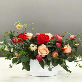 Mixed bouquet of roses and red carnations in a white container