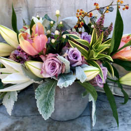 Low centerpiece of pink tulips, lavender roses, and white lilies in a gray pot
