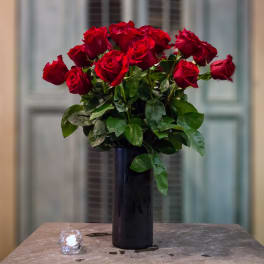 Red roses arranged in a tall black vase with a small candle nearby