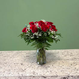 Arrangement of red roses with white filler flowers in a clear glass vase on a stone countertop