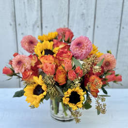 Bouquet of pink and orange roses with yellow sunflowers in a glass vase