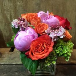 Bouquet of orange and pink roses with purple blooms in a glass vase