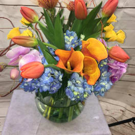 Colorful bouquet with tulips, calla lilies, orchids, and blue hydrangeas in a glass vase