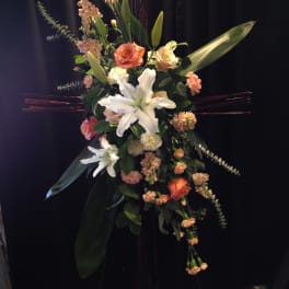 Standing floral spray with white lilies and peach roses on a dark easel