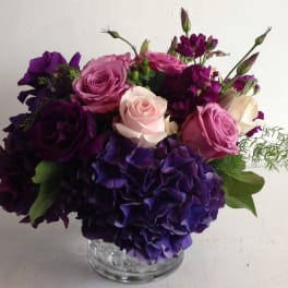 Purple and pink roses with hydrangeas in a clear glass vase