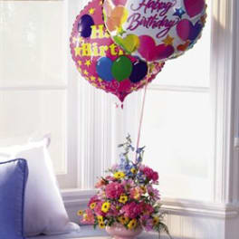 Birthday balloons above a pink flower arrangement in a vase