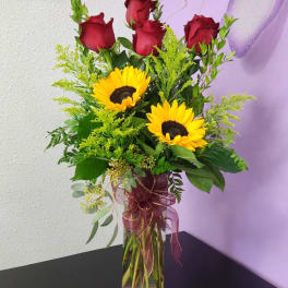 Red roses and sunflowers in a clear glass vase with ribbon