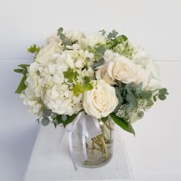 White rose and hydrangea bouquet in a glass vase with ribbon