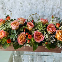 Long low floral arrangement with pink and orange roses in a wooden box
