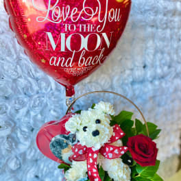 Heart-shaped red balloon above a basket with white flowers and a red rose