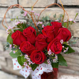 Red roses arranged in a glass vase with a heart-patterned ribbon
